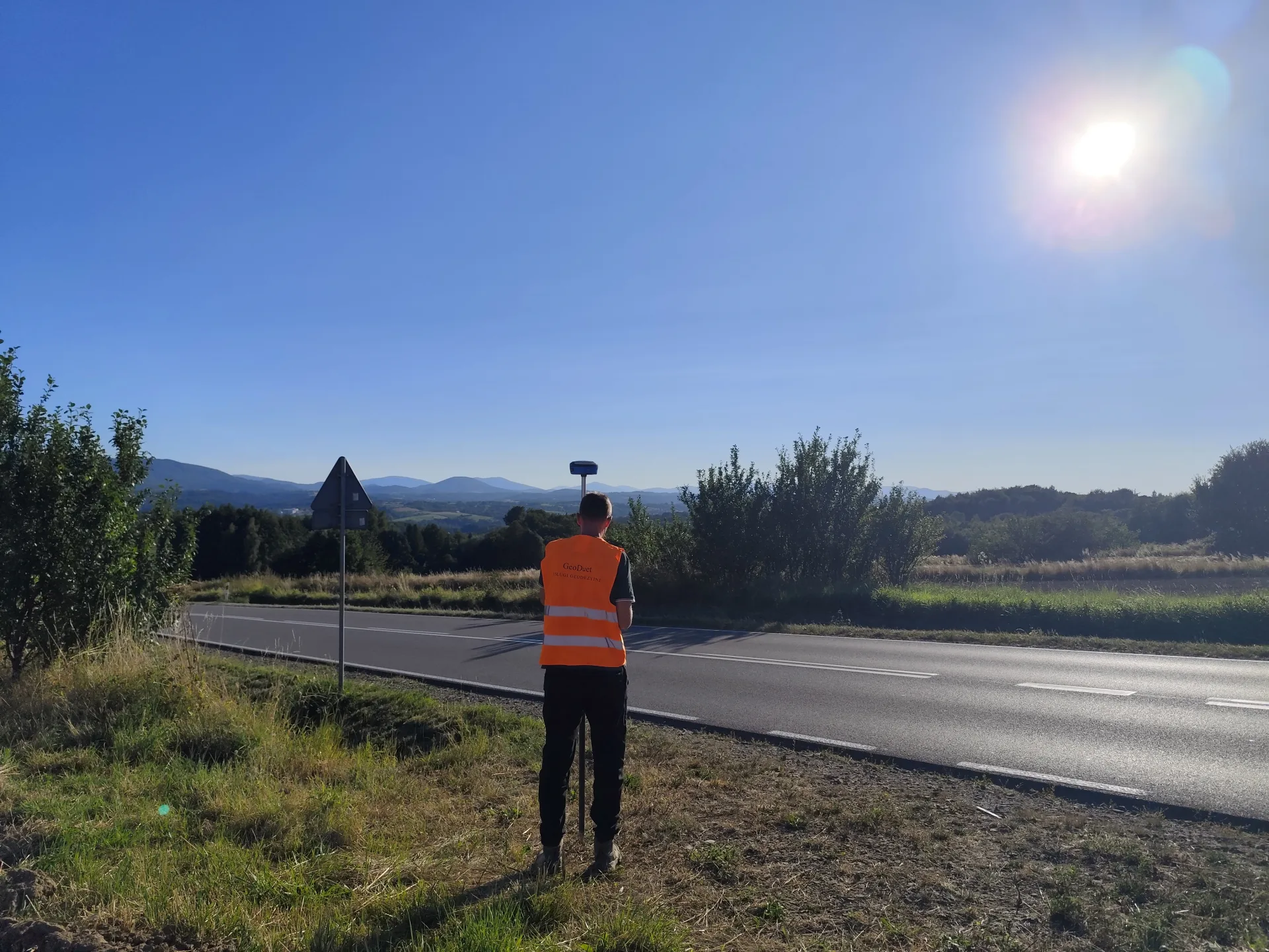 Geodeta wykonujący pomiar odbiornikiem GNSS przy drodze
