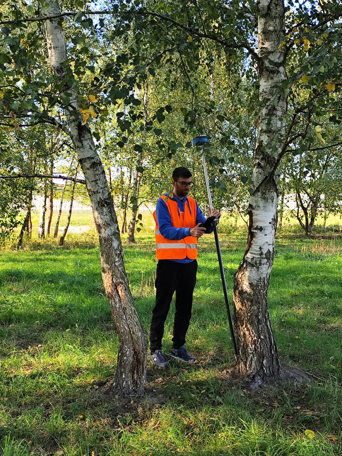 Geodeta GeoDuet z odbiornikiem GNSS podczas pomiaru wśród drzew