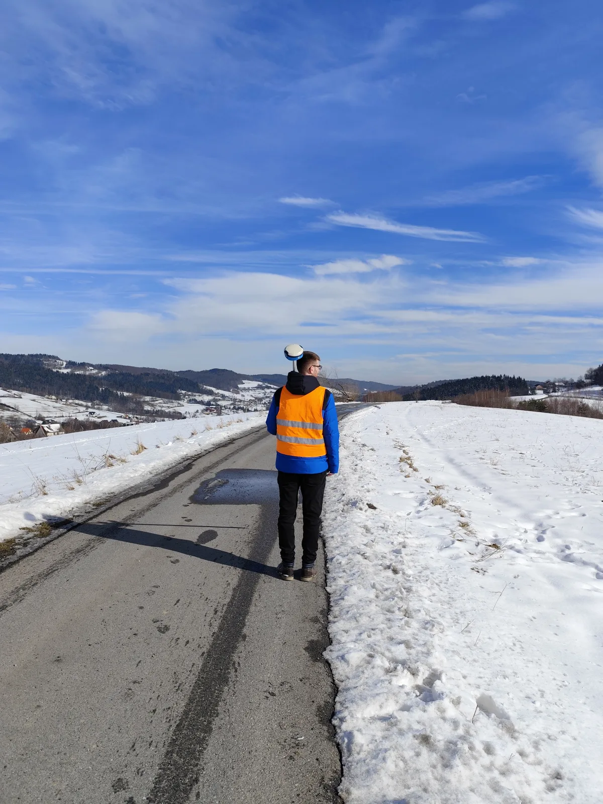 Geodeta z odbiornikiem GNSS na zimowej drodze